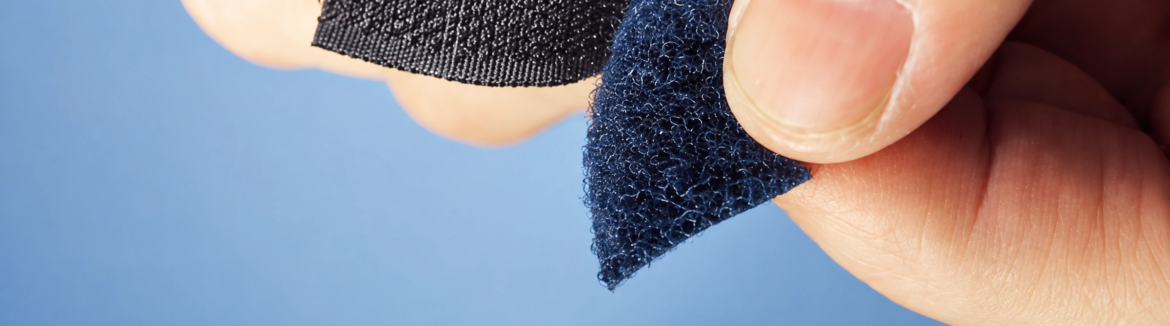 Hand pulling apart a strip of black hook-and-loop velcro fastener against a blue background