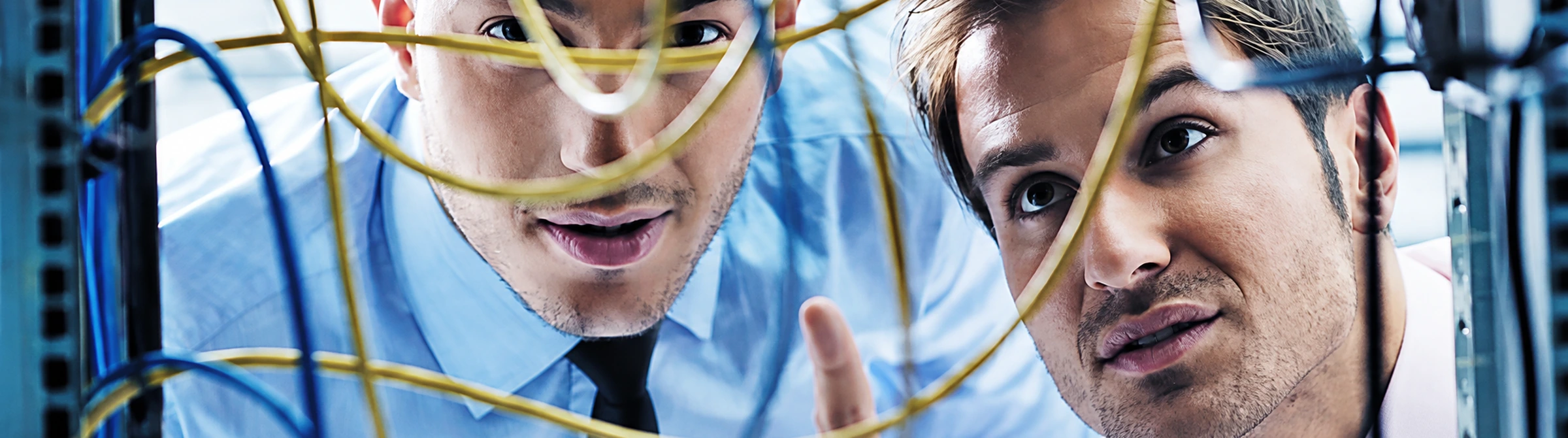 Two IT professionals viewed through a tangle of coloured network cables in a server room